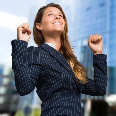 Petra Sommerfeld – Soul- & Self-Leadership Unternehmerinnen Hoer auf zu funktionieren - fang an zu sein Eine strahlende Unternehmerin im dunklen Nadelstreifen-Blazer blickt lächelnd mit geballten Fäusten nach oben vor einer modernen Business-Skyline, befreit von alten Mustern und lebt tiefes Self-Leadership.